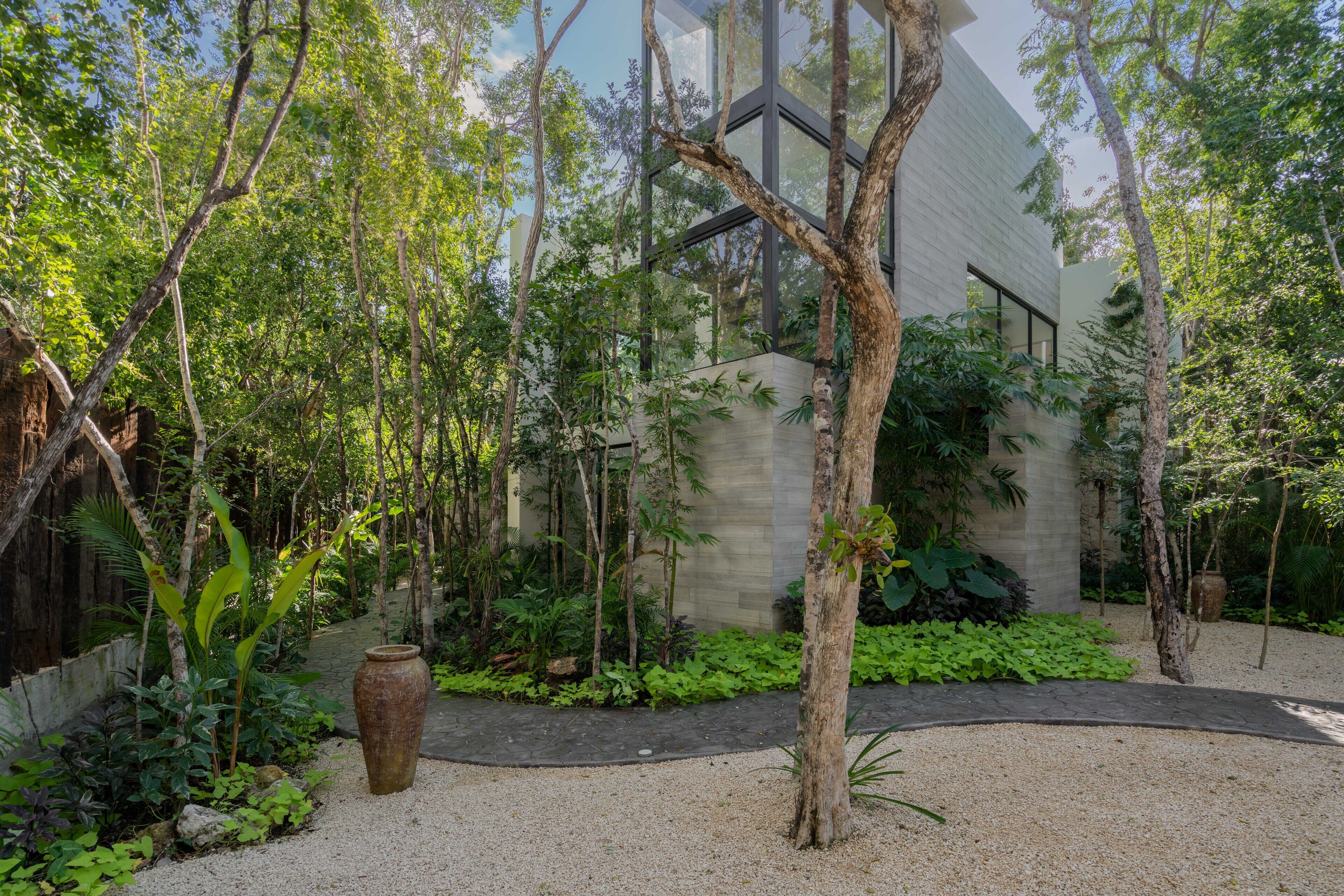 A modern building with a glass facade surrounded by dense greenery and a gravel pathway.
