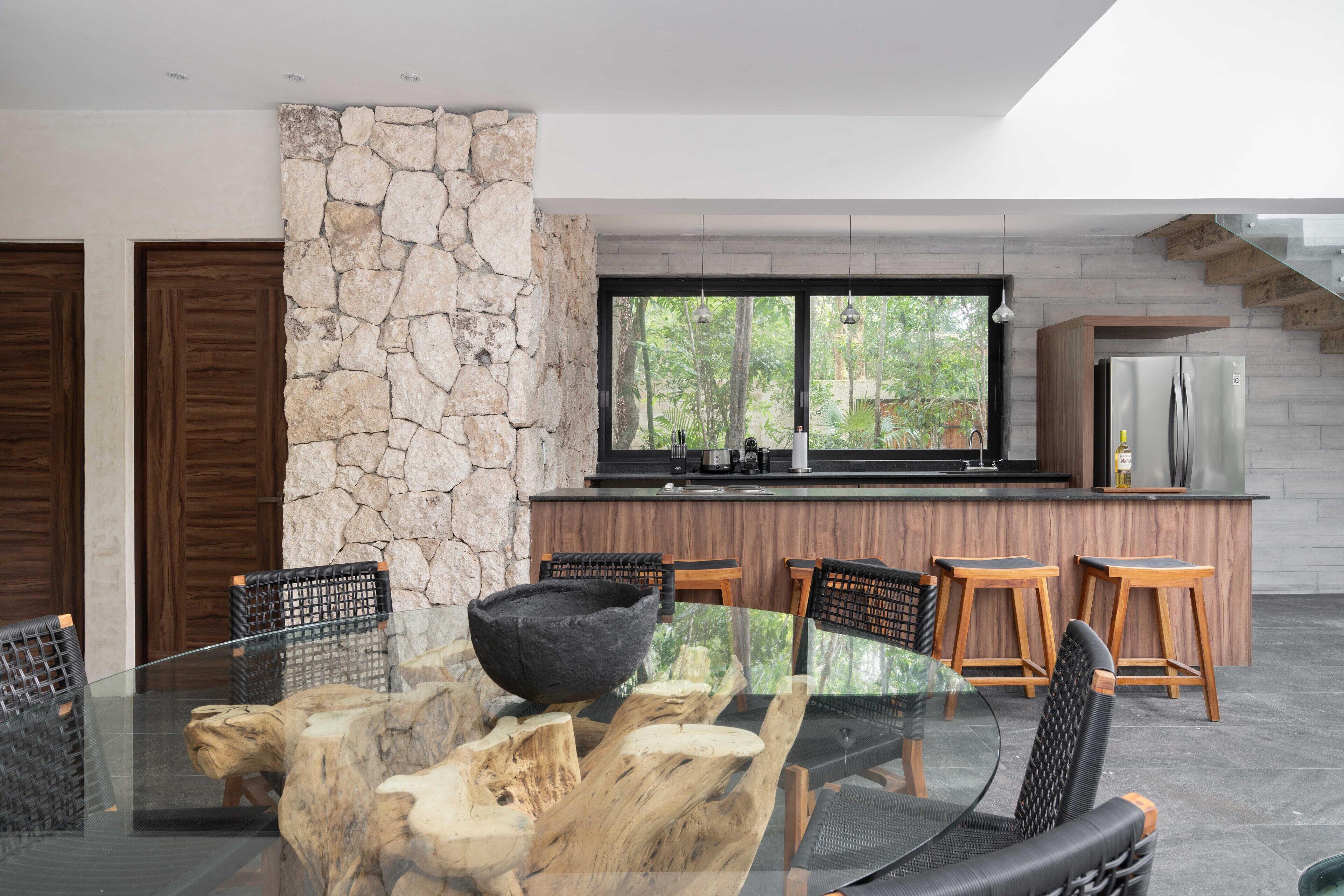 A modern kitchen with a stone accent wall, wooden bar stools, and a glass dining table.