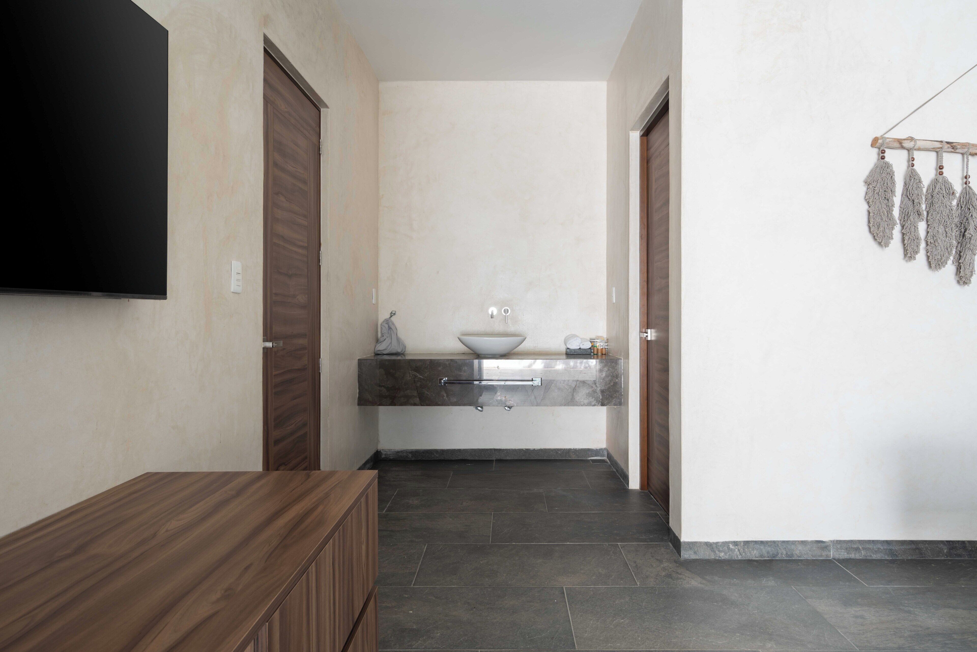 A narrow hallway with a wooden bench, a marble sink, and a wall-mounted television.