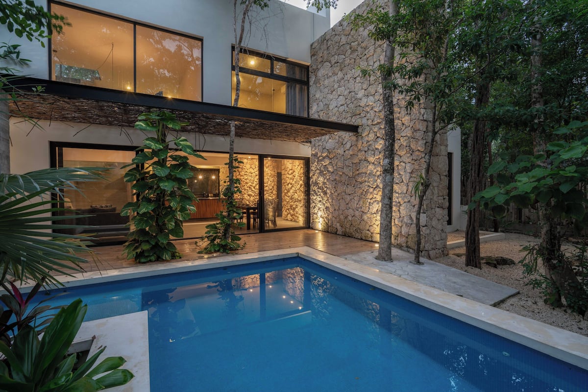 A modern house with a swimming pool, stone walls, and indoor lighting.