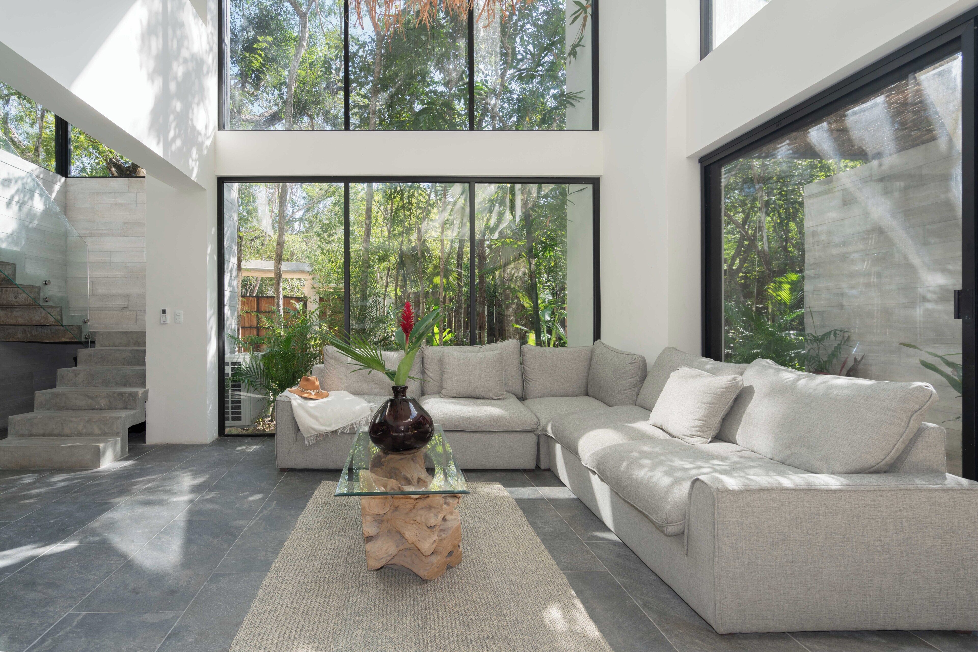 A modern living room with a glass coffee table, a beige sofa, and a staircase.