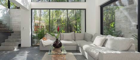 A modern living room with a glass coffee table, a beige sofa, and a staircase.