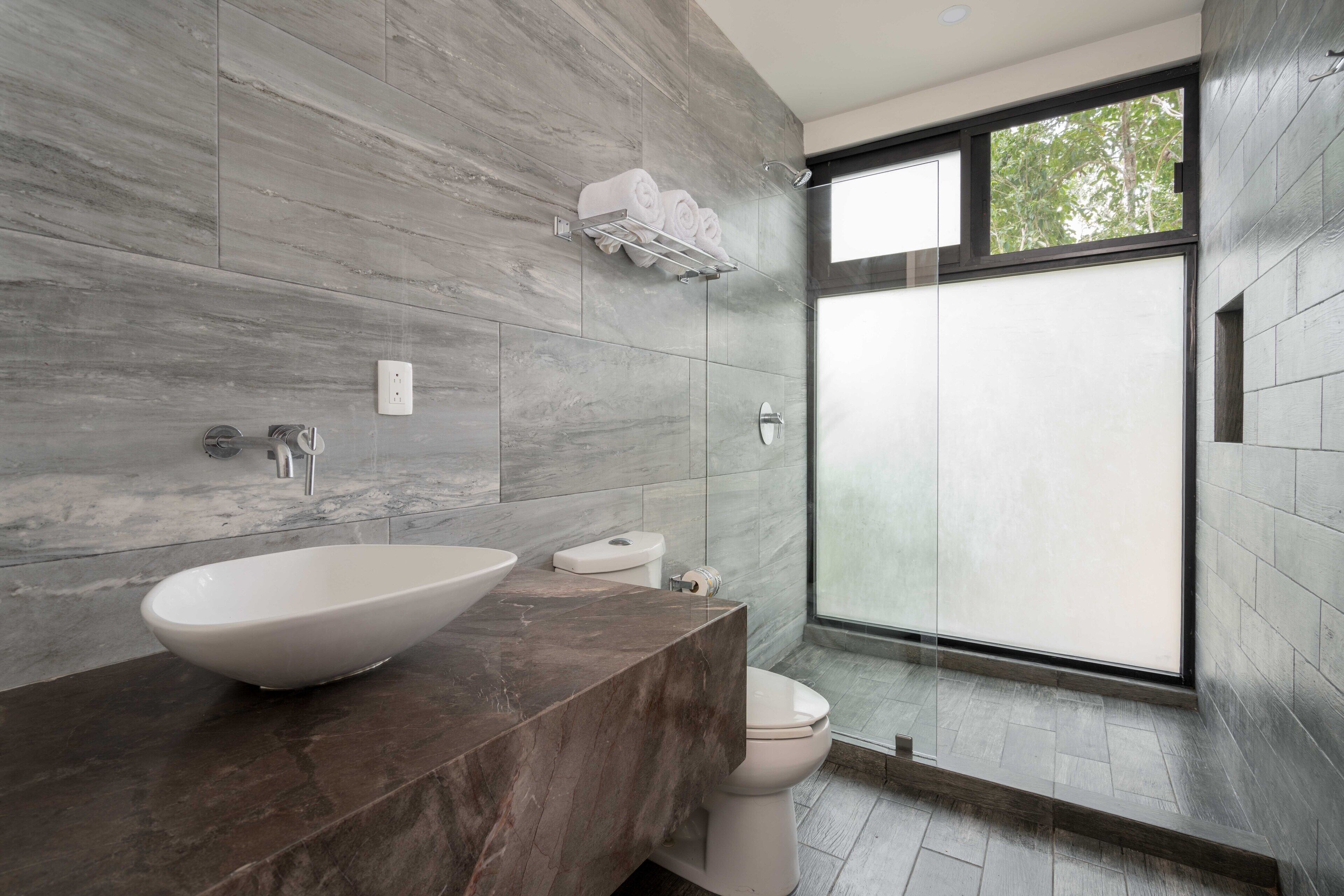 A modern bathroom with a large vessel sink, a toilet, and a shower area.