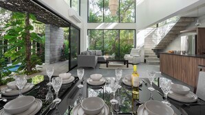 A modern dining area with a glass table, white plates, and wine glasses, overlooking a lush garden and a staircase. - Twelve O’Clock Luxury Villas (Tulum)