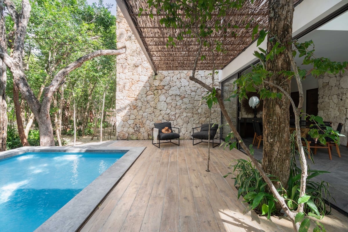 A poolside area with a stone wall, wooden deck, and two lounge chairs.