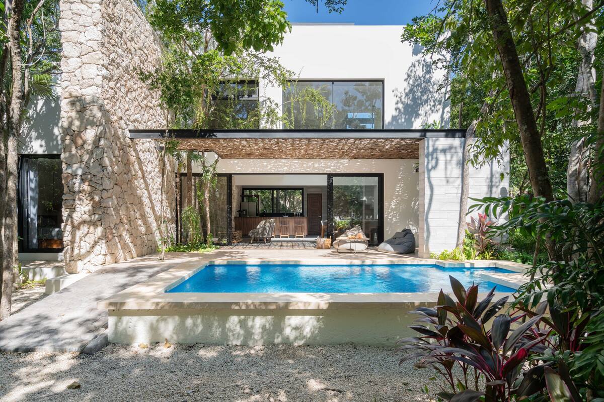 A modern house with a swimming pool, stone walls, and a patio area with outdoor furniture.