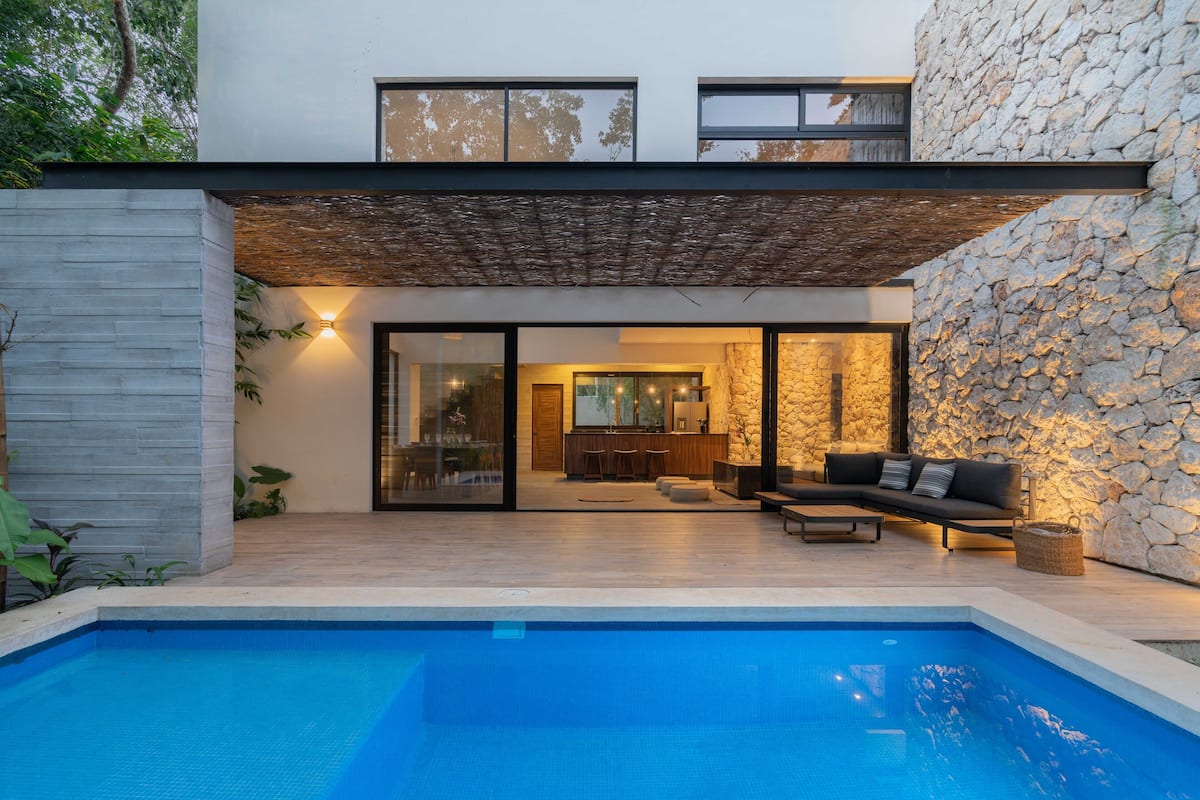 A modern house with a swimming pool, stone walls, and a patio area with outdoor furniture.