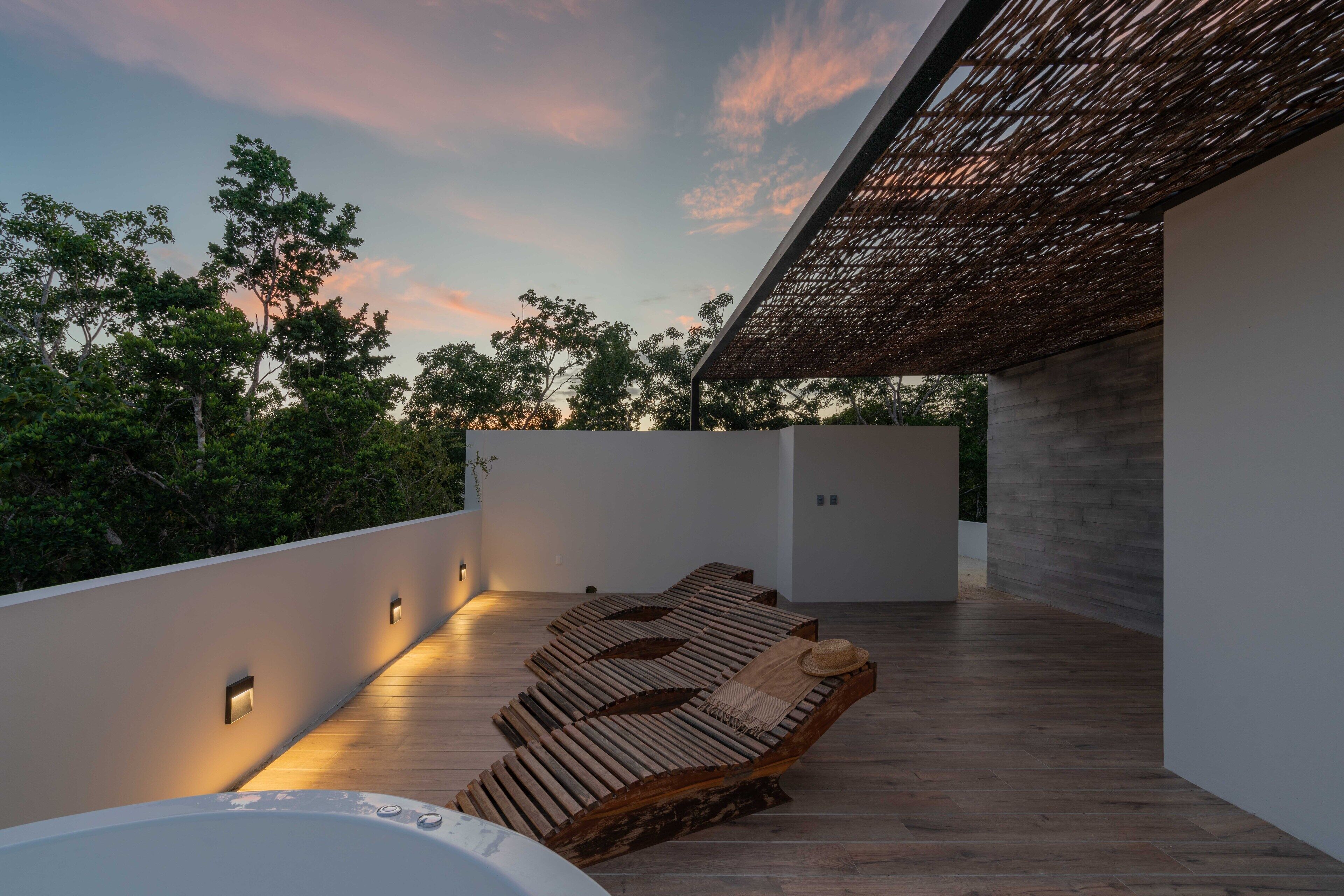 A rooftop terrace with wooden loungers, a hot tub, and a view of trees and sky.