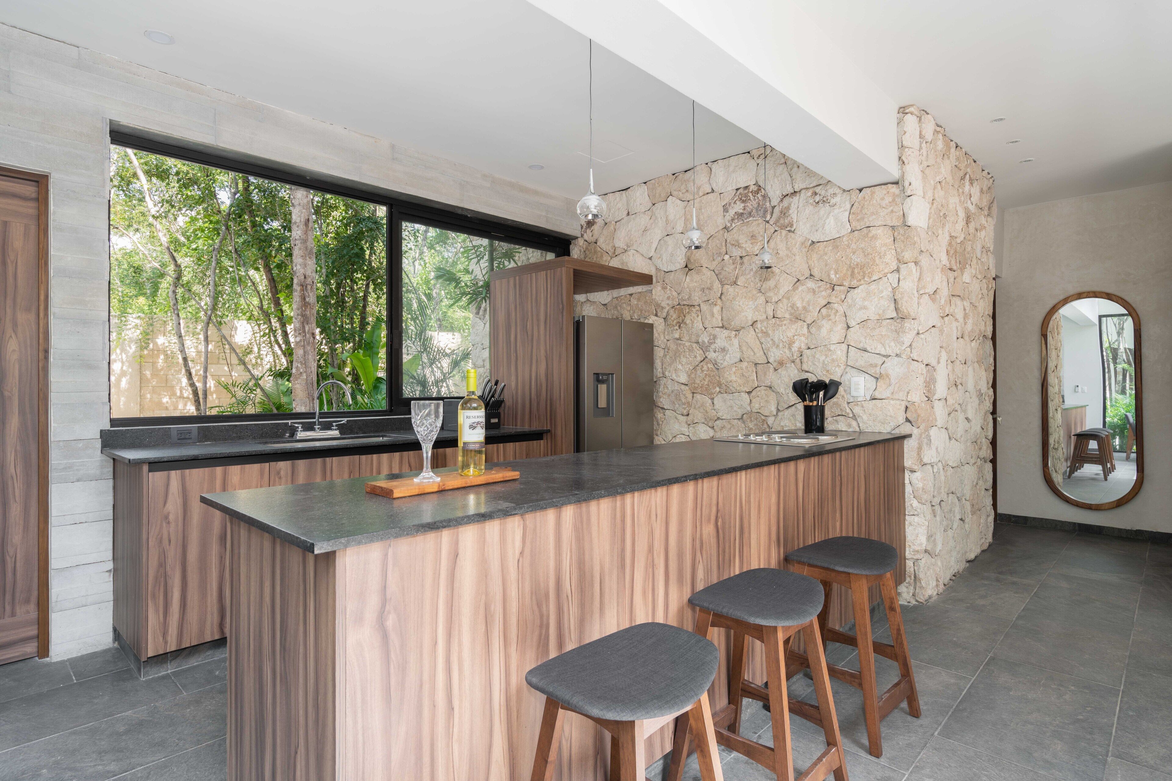 A modern kitchen with a large island, bar stools, and a stone accent wall.