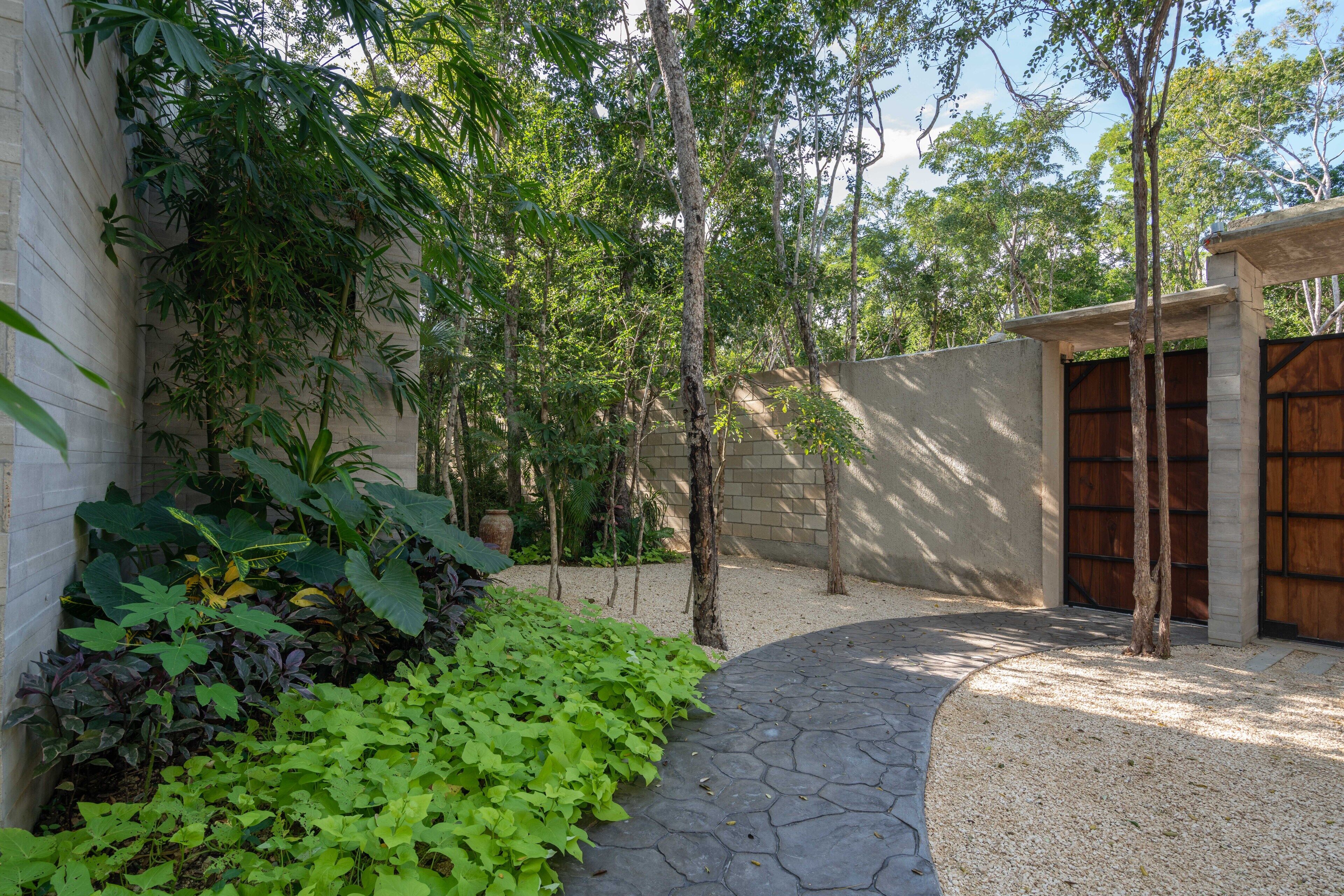 A courtyard with a stone pathway, greenery, a wooden gate, and a brick wall.