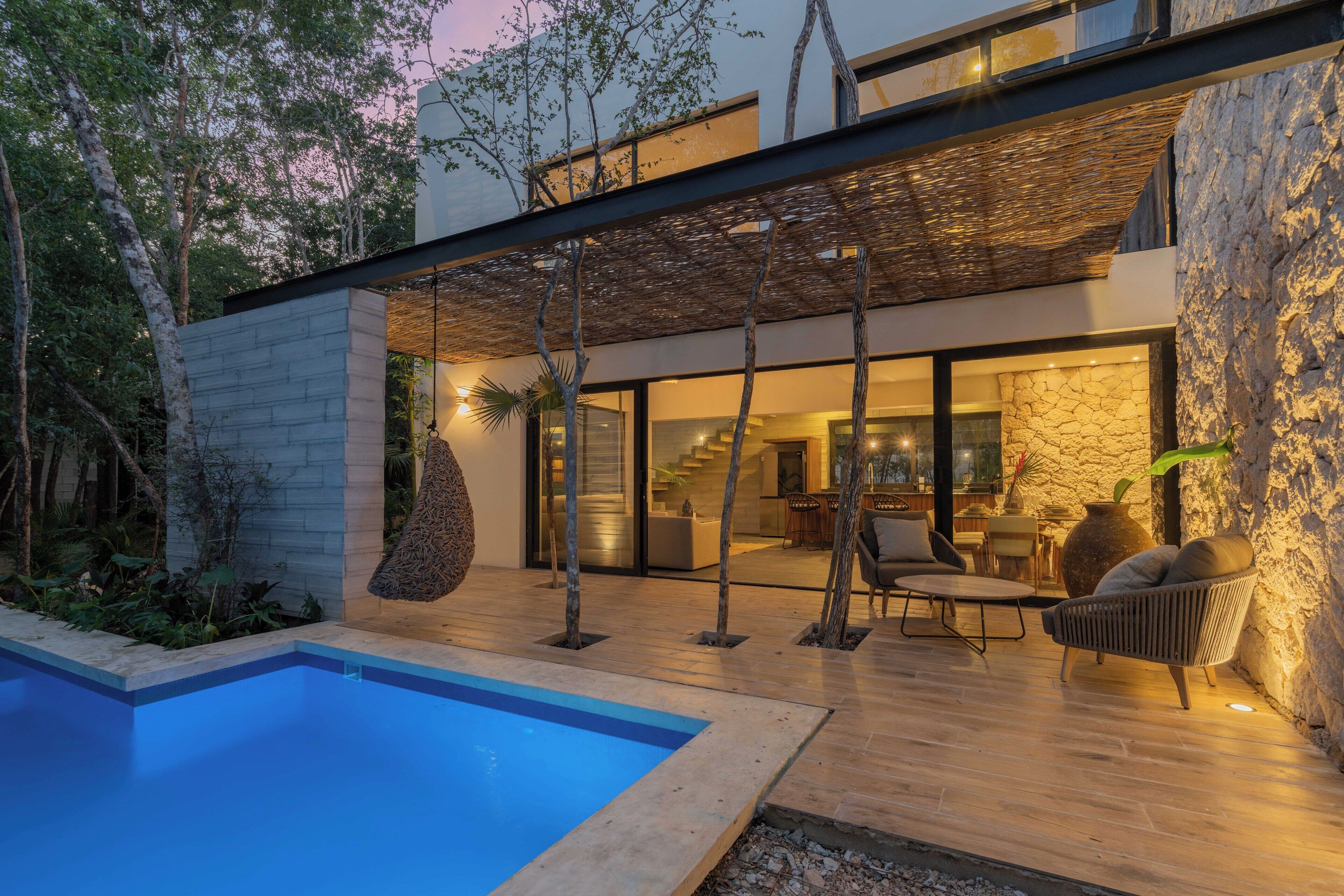 A modern house with a swimming pool, outdoor seating, and a stone wall.