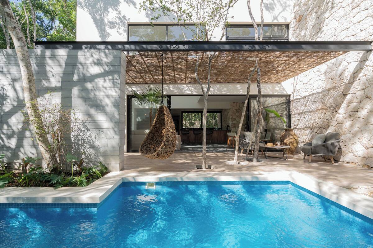 A modern outdoor pool area with a clear blue pool, a hanging swing, and a stone wall backdrop.
