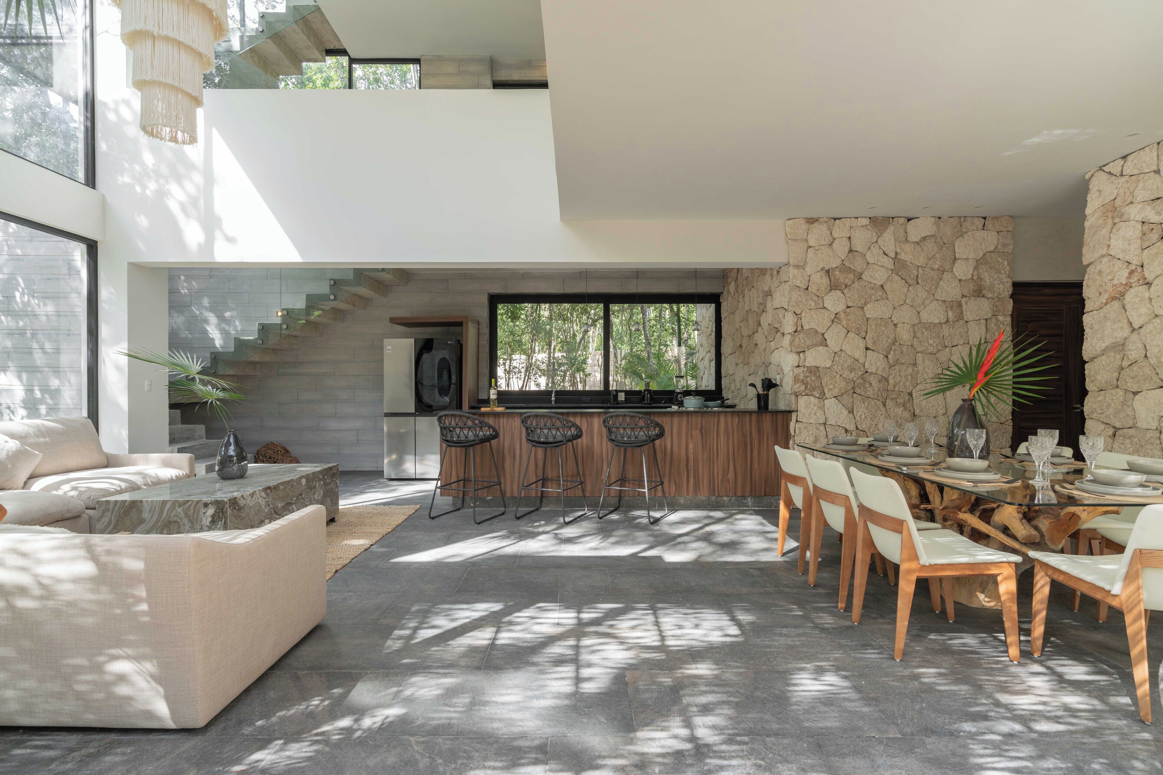 A modern living area with a stone wall, a dining table with chairs, and a staircase leading to an upper level.