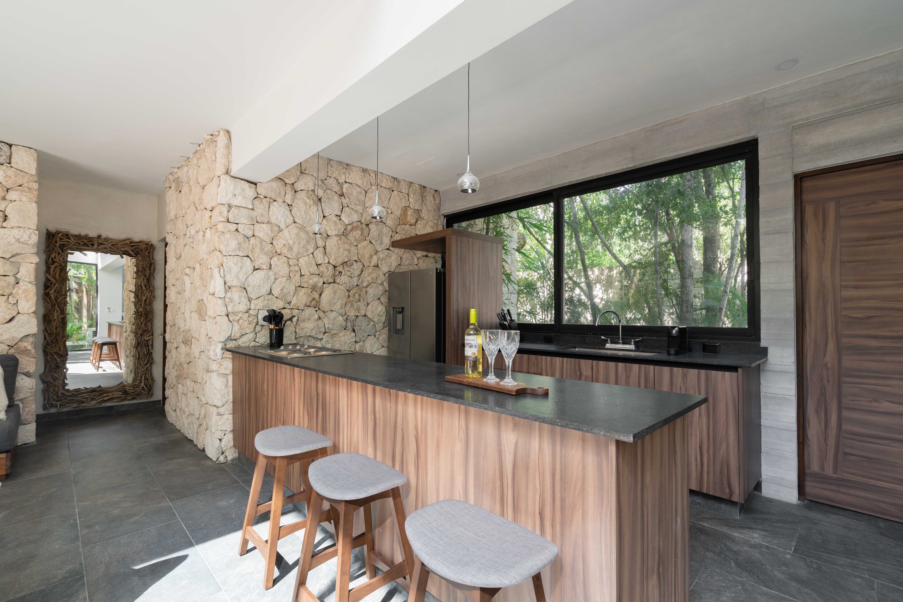 A modern kitchen with a stone accent wall, a large window, and a bar area with stools.