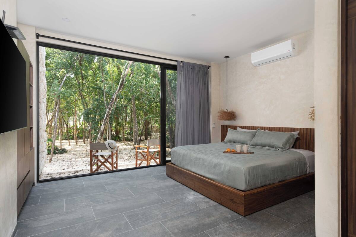 A bedroom with a large sliding glass door leading to an outdoor area, a bed with a wooden frame, and a ceiling-mounted air conditioning unit.