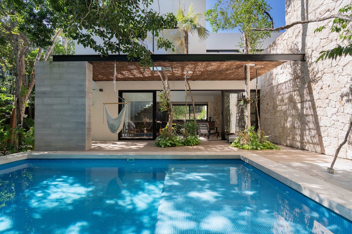 A modern house with a swimming pool, a hammock, and a stone wall.