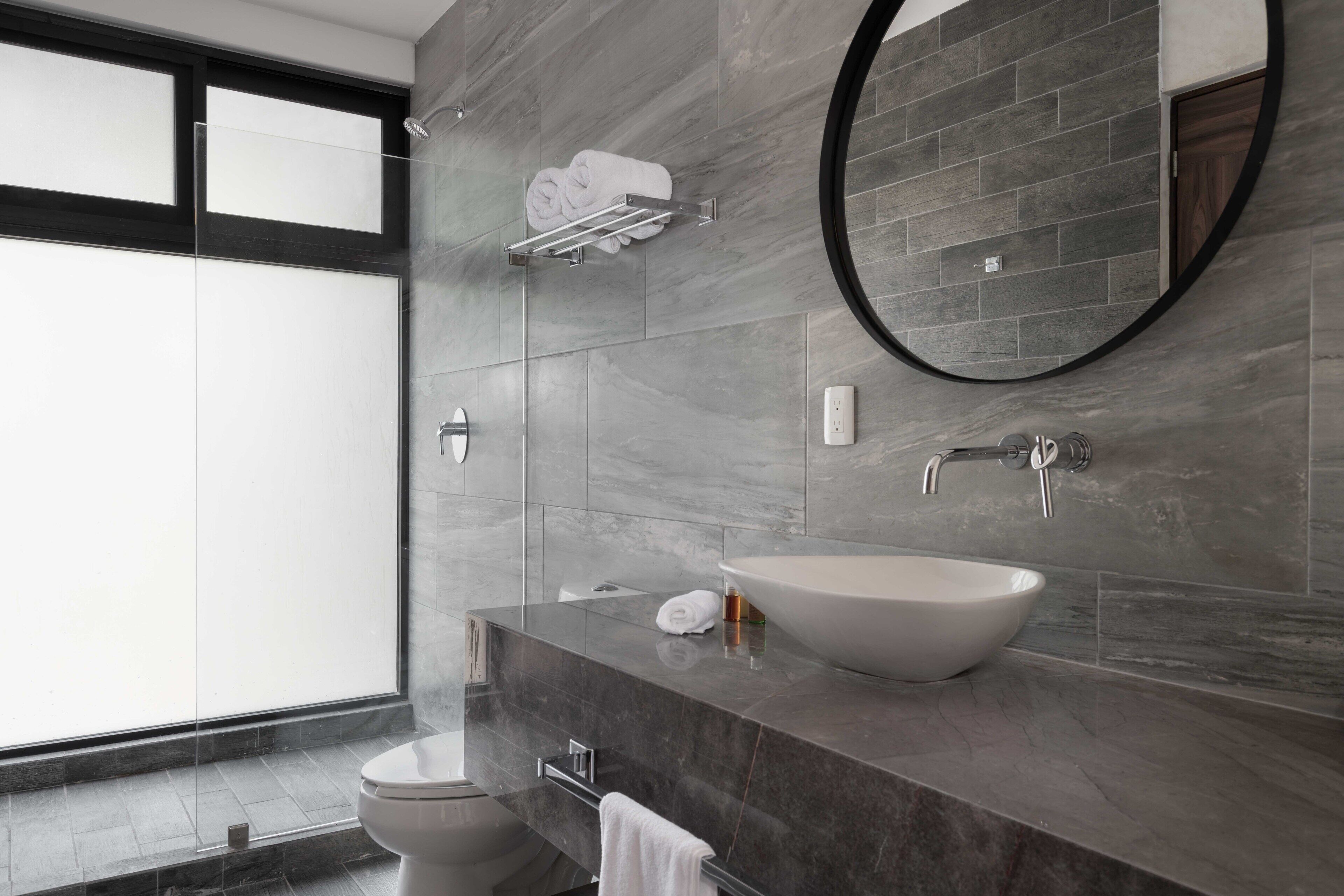 Un baño moderno con un ventanal grande, un espejo redondo, un lavabo de pedestal y un perchero para toallas.