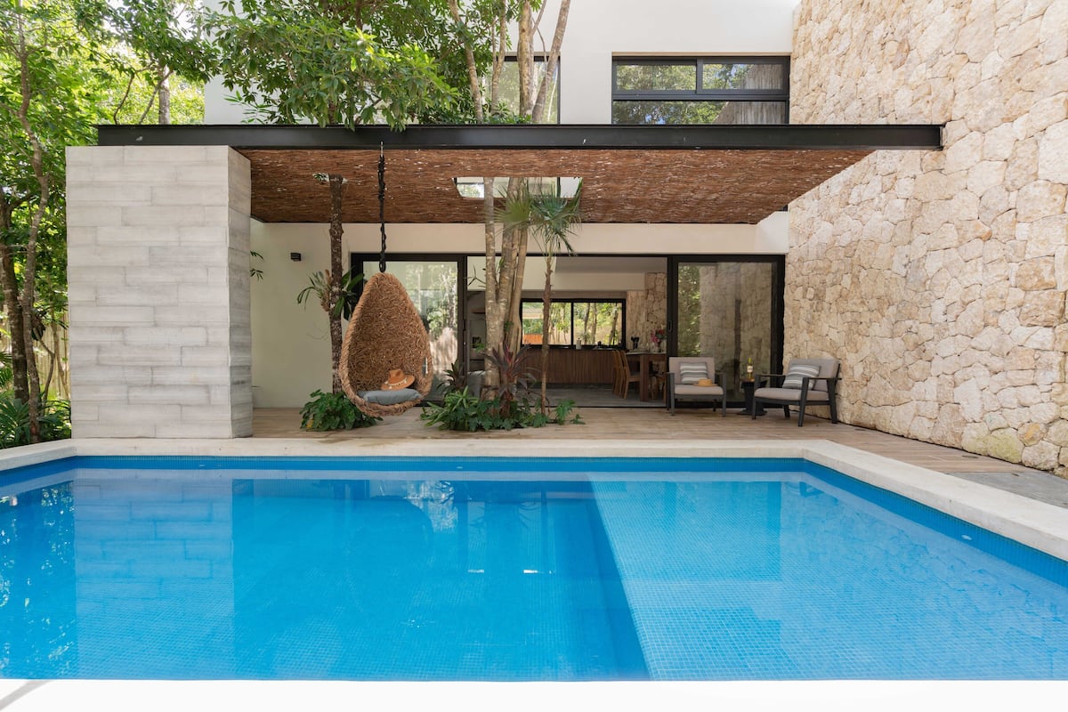 A modern house with a swimming pool, stone walls, and a hanging chair.