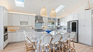A modern kitchen with white cabinets, a central island with chairs, a large window, and a skylight. - Smiling Otter Retreat! Large Lakefront Luxury House.Pool.Spa.Sauna.Games..Pets (Clearlake)