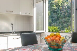 A kitchen with a window view of a forest, a sink, and a fruit bowl on the table.
