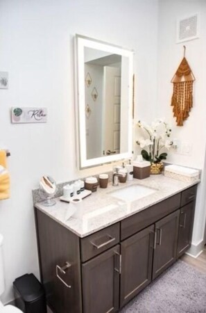 A modern bathroom with a double sink vanity, dark wood cabinets, a large mirror, and decorative wall hangings.
