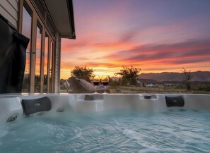 A hot tub with a sunset view, a house in the background, and mountains in the distance.
