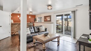 A living room with a dark leather sofa, a wooden coffee table, and a sliding glass door leading to an outdoor area. - Mid-Farmers Park (Colorado Springs)