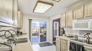 A kitchen with a double sink, a stove, and a microwave. There is a sliding glass door leading to a balcony. - Mid-Farmers Park (Colorado Springs)
