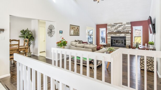 A spacious living area with a fireplace, a ceiling fan, and a white railing. - Mid-Farmers Park (Colorado Springs)