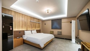 A modern hotel room with a large bed, a built-in TV, a minibar, and a ceiling light fixture. - kkaebistay (Pohang)