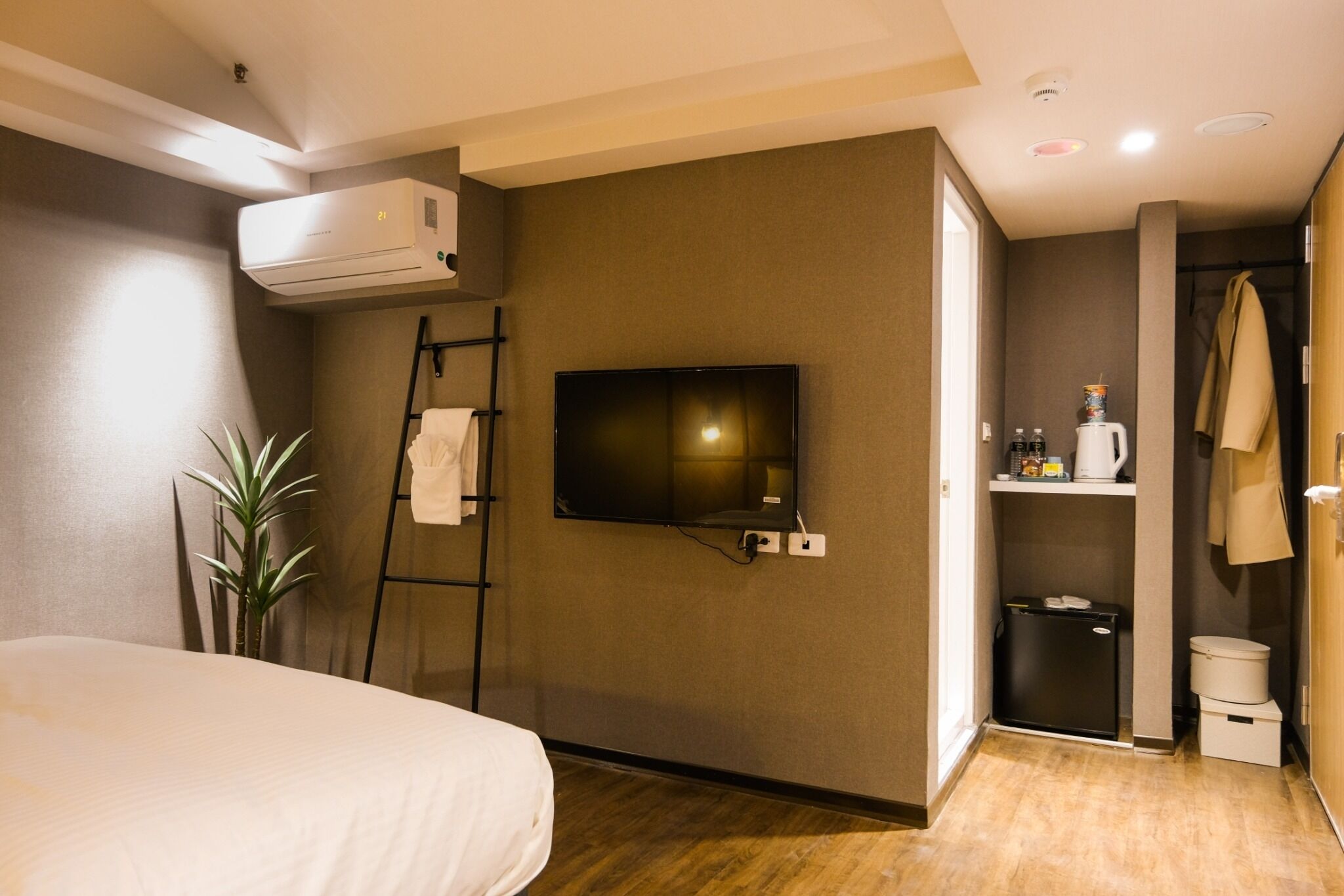 Habitación de hotel con cama, televisión montada en la pared, un cubo de basura pequeño y un perchero para toallas.
