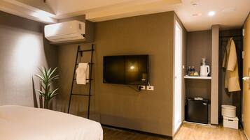 Habitación de hotel con cama, televisión montada en la pared, un cubo de basura pequeño y un perchero para toallas.
