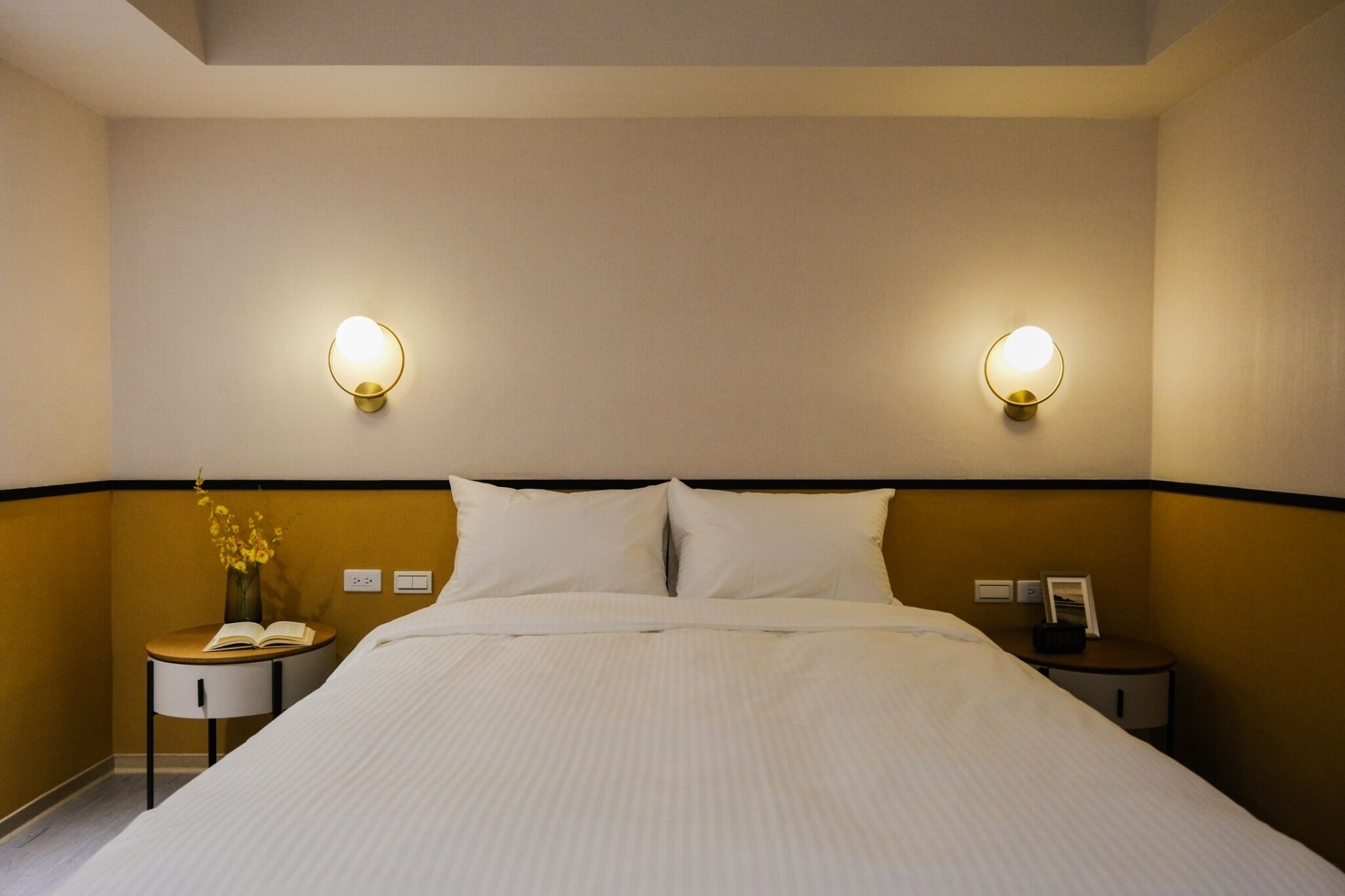 A hotel room with a large bed, two bedside tables, a nightstand, and wall-mounted reading lights.