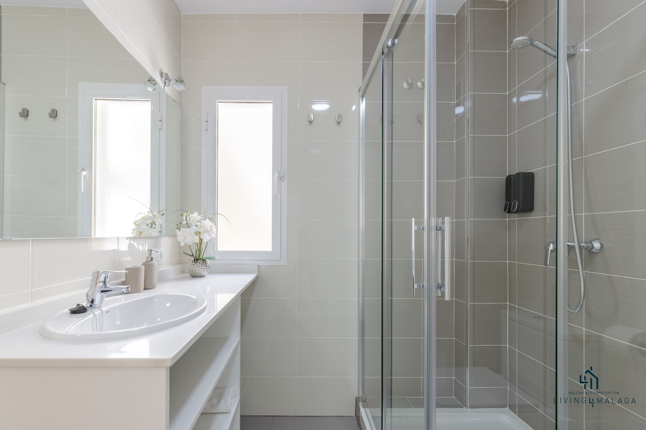 Un baño moderno con ducha de vidrio, lavabo blanco y un espejo grande.