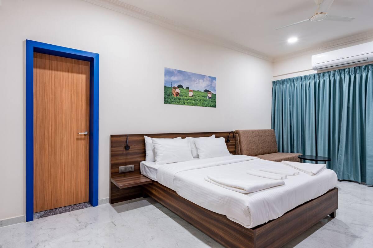 A modern bedroom with a wooden bed, a nightstand, a wall-mounted air conditioner, and a painting of a field.