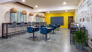 Un comedor moderno con sillas azules, mesas y lámparas colgantes de mimbre.