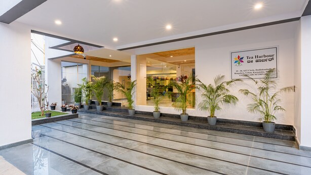 Entrada moderna de un edificio con letrero de Tea Harbour, que presenta una puerta de vidrio, plantas en macetas y una escalera que conduce al interior.
