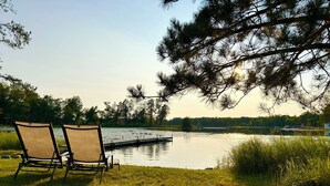 Two chairs facing a lake with a dock and a grassy area.