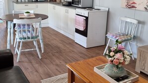A modern kitchen with white cabinets, a microwave, and a stove. There is a dining table with chairs and a coffee table with a vase of flowers.