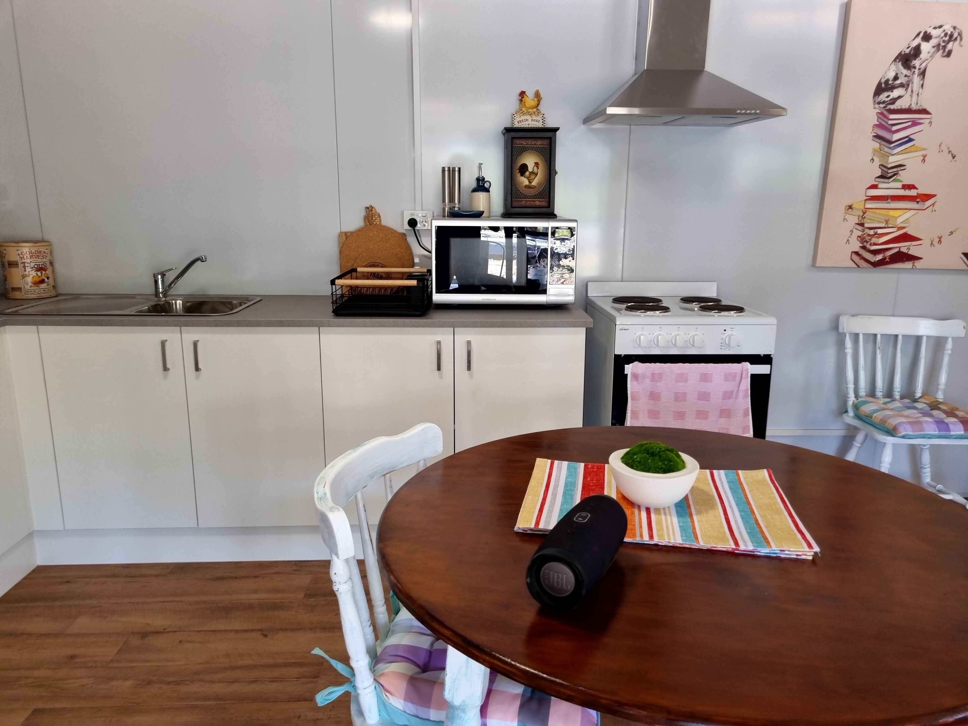 Une cuisine avec des meubles blancs, un four à micro-ondes, une cuisinière et une table à manger sur laquelle se trouve un saladier rempli d’aliments verts.