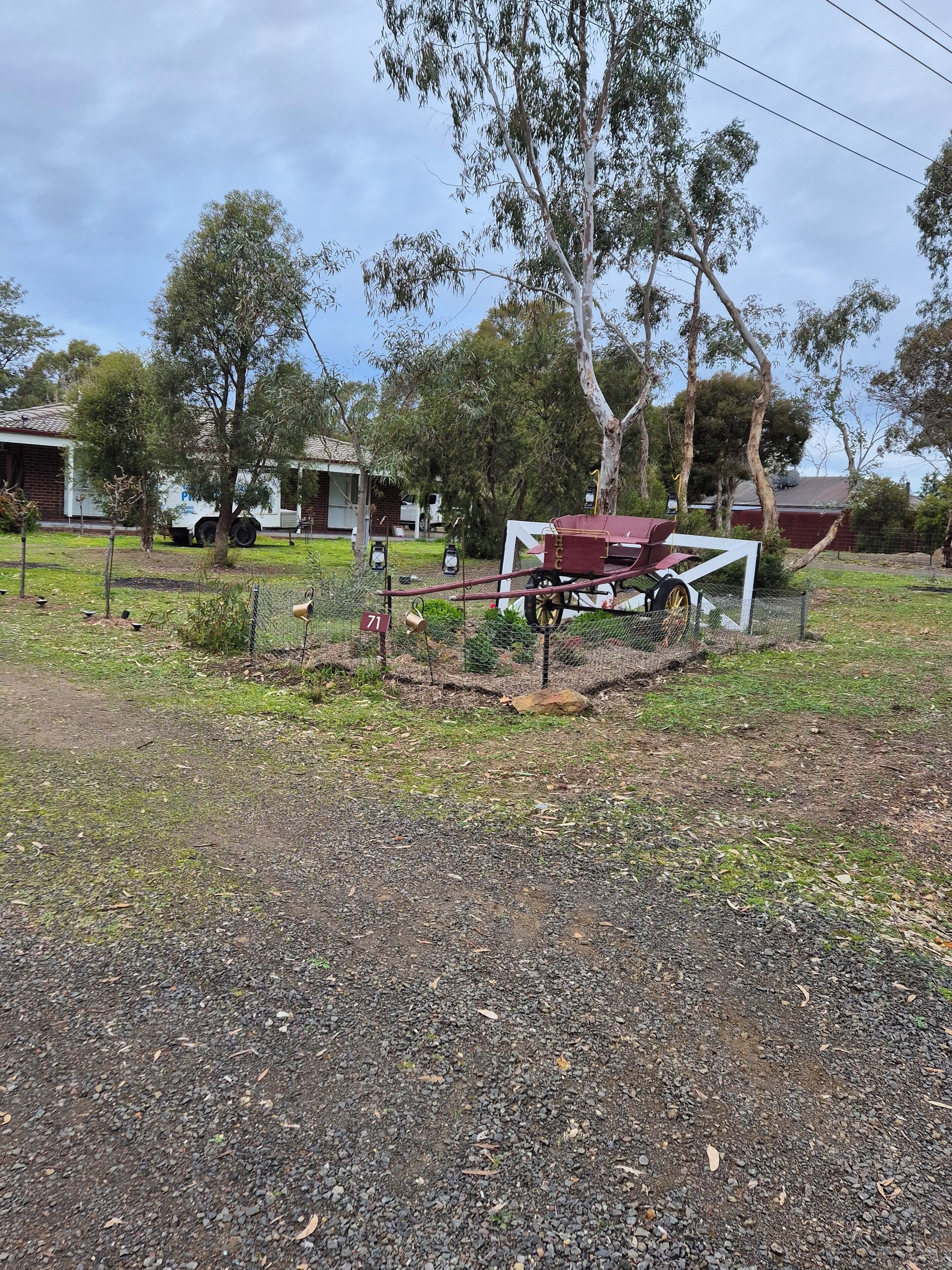 A rural property with a gravel driveway, a fenced area with a horse-drawn cart, and a building in the background.
