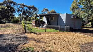 A small, single-story mobile home with a porch and a fenced yard.