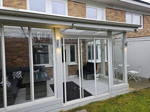 A covered patio area with a glass enclosure, outdoor seating, and a brick wall in the background. - 3Br House, Sleeps 7 with Balcony-Garden-Bbq-FreeP (Malmo)