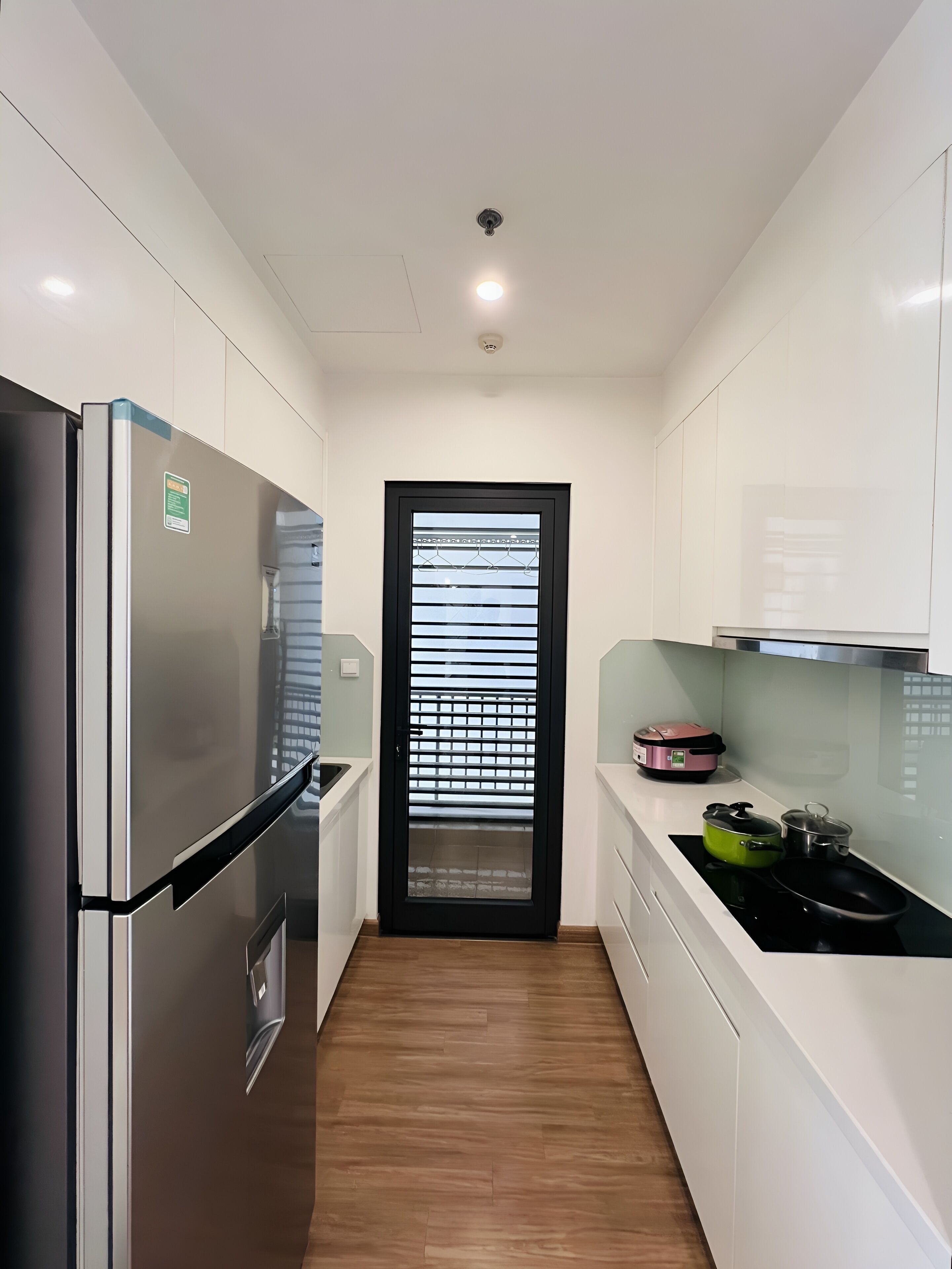 A modern kitchen with white cabinets, a stainless steel refrigerator, a black-framed door, and a countertop with a rice cooker and pots.