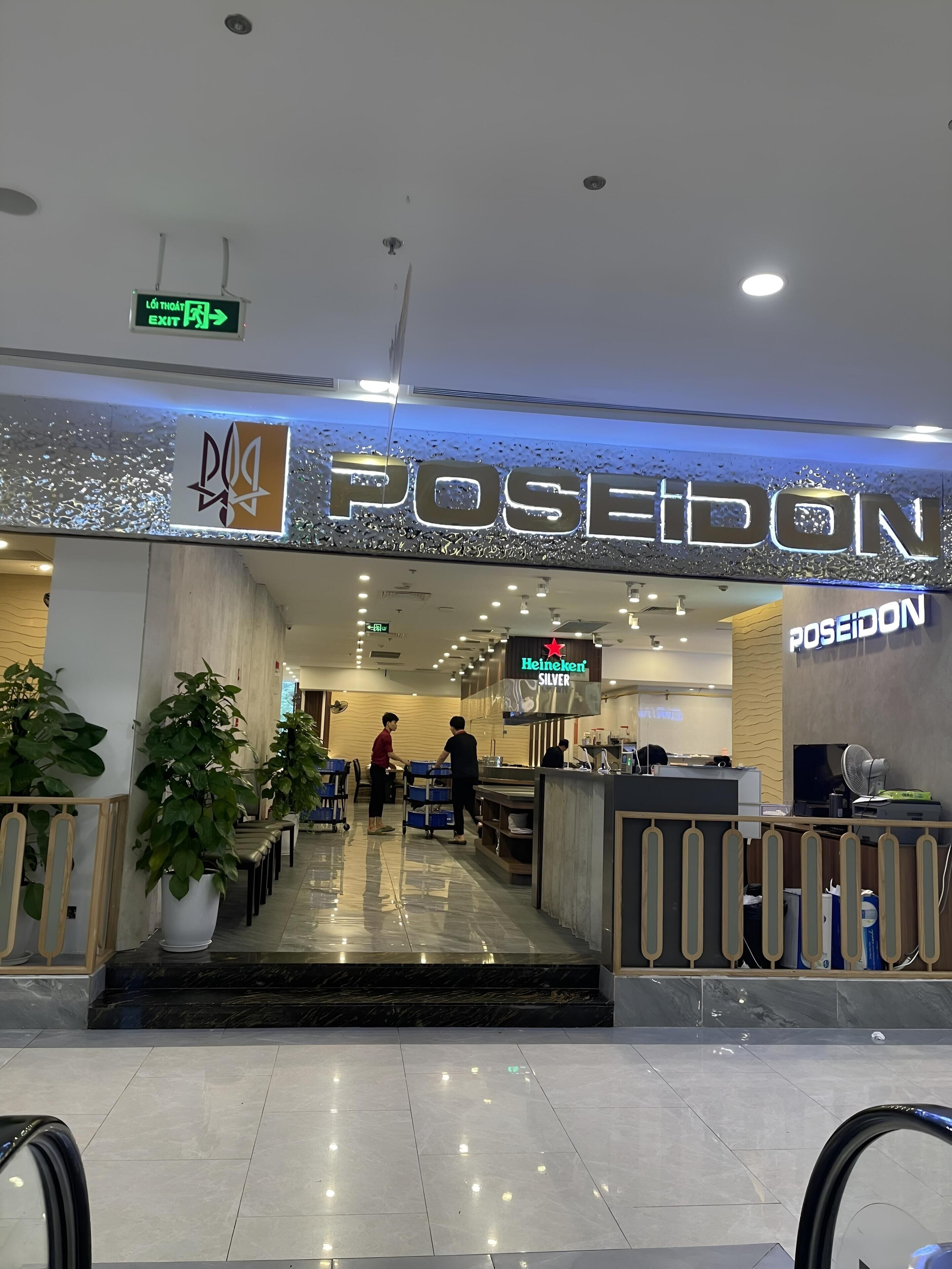 L’entrée de Poseidon, un restaurant au design moderne, se distingue par une enseigne bien visible et un espace où sont disposées des tables et des chaises.