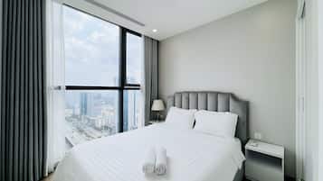 Una habitación de hotel moderna con una cama grande, una mesita de noche, una lámpara y vistas a la ciudad a través de amplios ventanales.