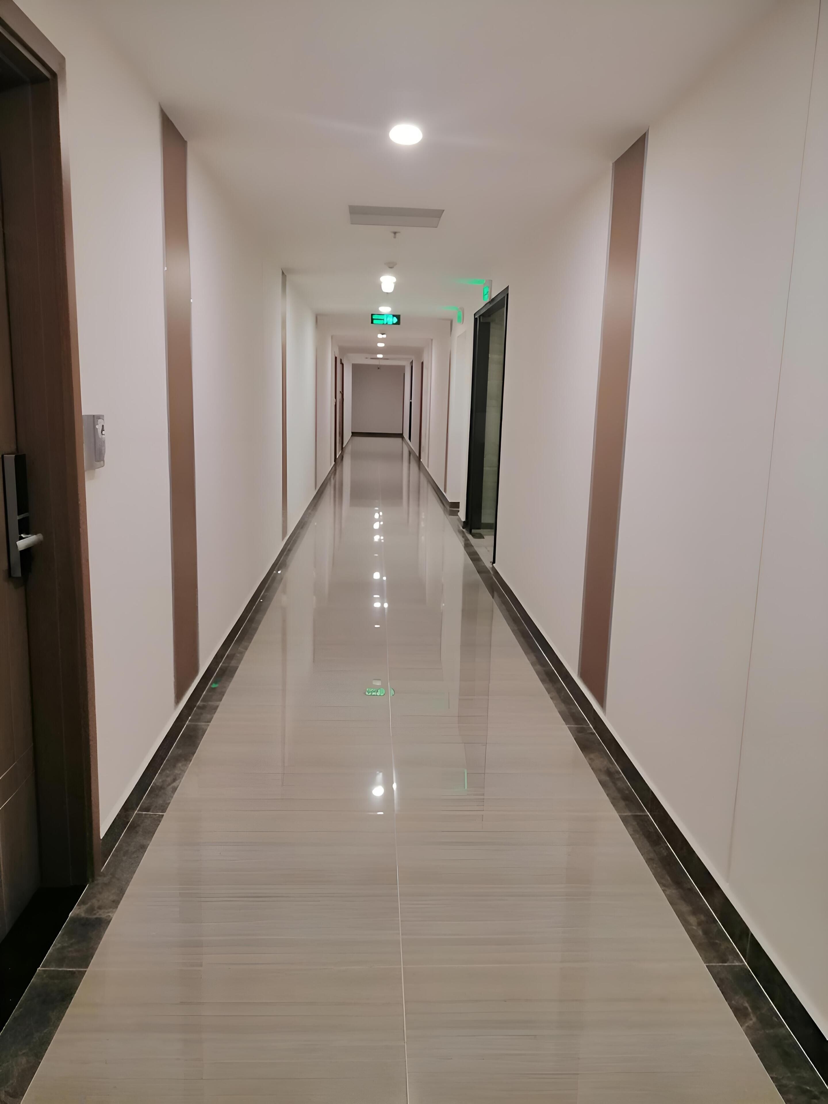 A long, well-lit hallway with a shiny floor, doors on both sides, and a ceiling light.