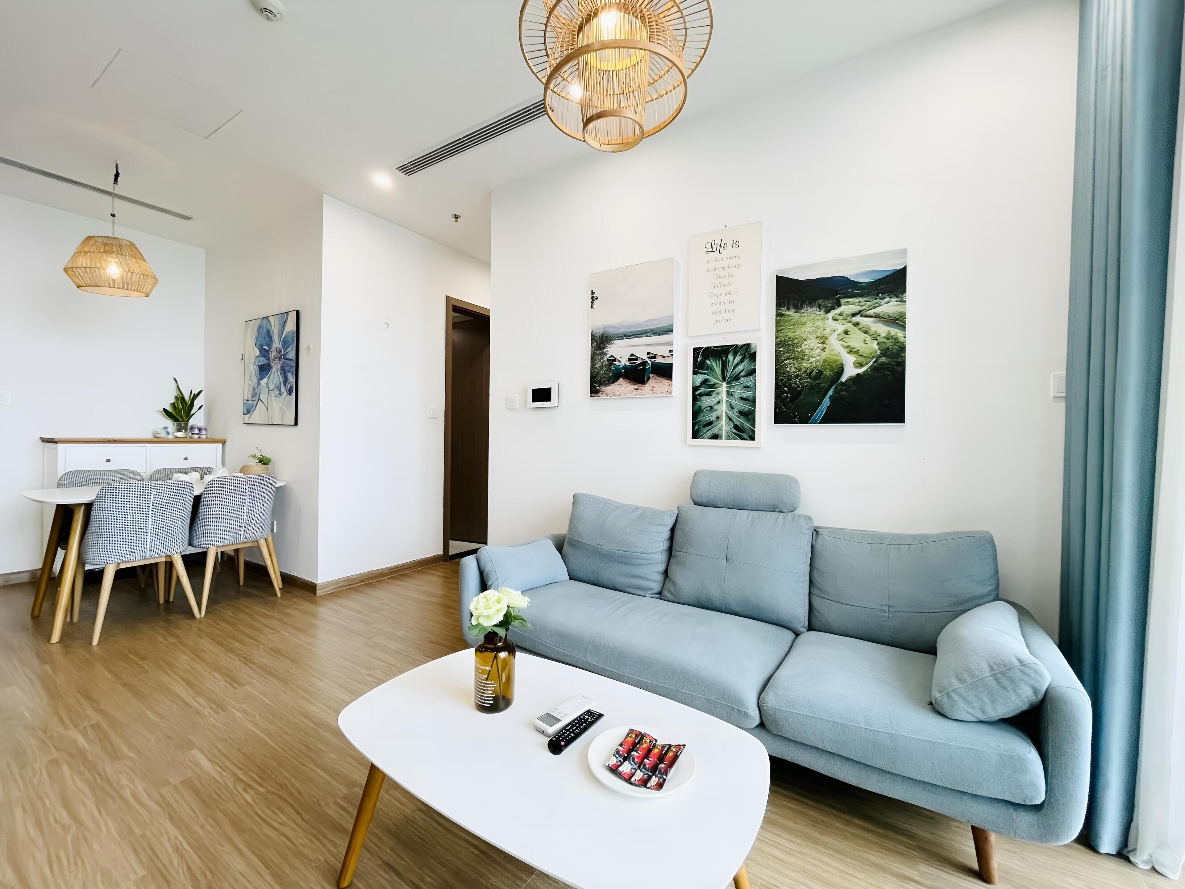 Un salon moderne avec un canapé bleu clair, une table basse blanche agrémentée d’un vase et d’une télécommande, et un coin repas avec une table et des chaises blanches.