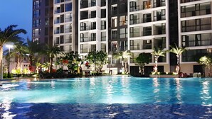 A swimming pool surrounded by palm trees and modern buildings with multiple floors and large windows.