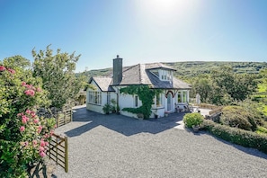 A white house with a sloped roof and a chimney, surrounded by gravel and greenery. - Elegant Holiday Cottage on the Banks of the River Artro | Artro (Llanbedr)